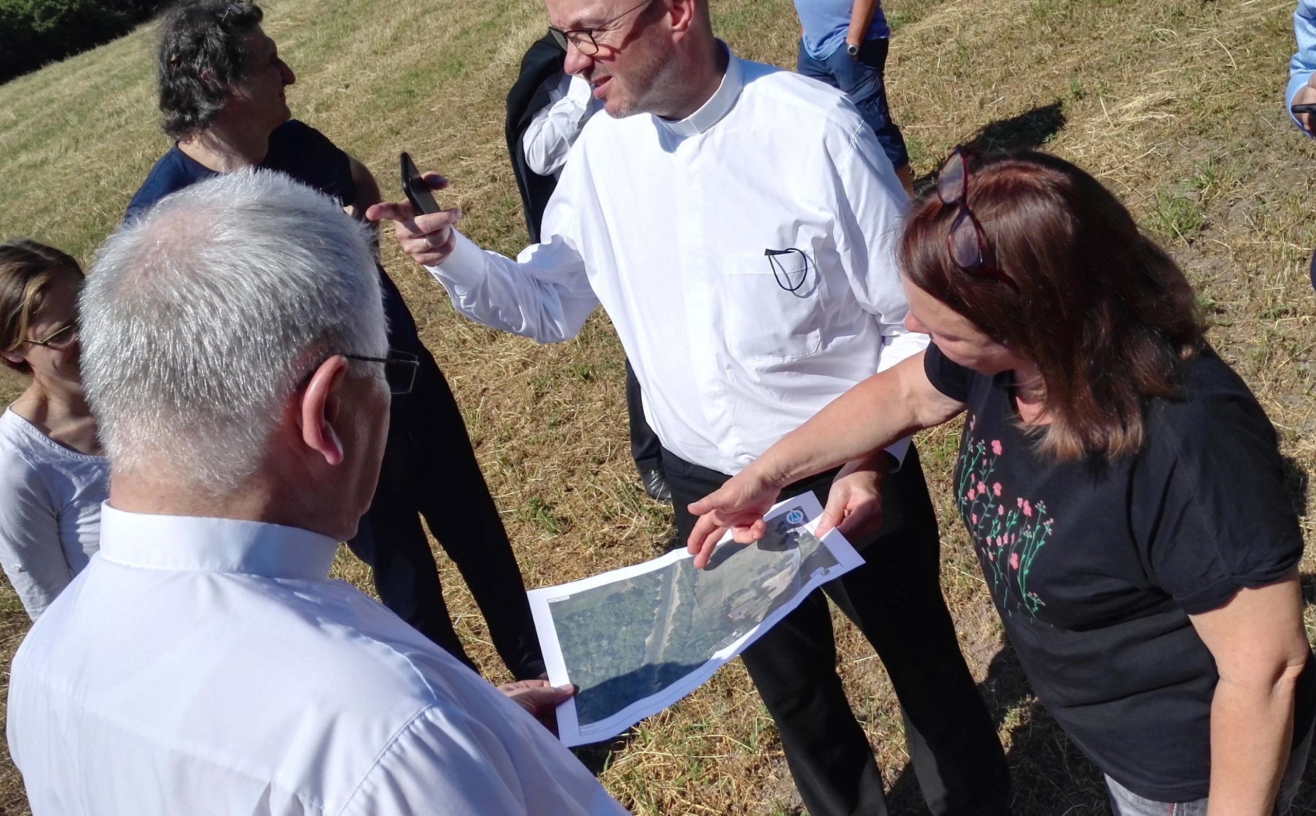 Eine Gruppe von Menschen auf einem Feld. Die Bischöfe tragen weiße Hemden. Rechts erklärt Conny Scheffler anhand einer Karte die Zukunftspläne.
